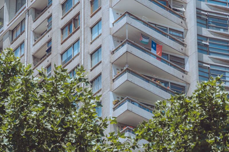 Edificio de departamentos en Santiago entre árboles, con una bandera de Chile en un balcón